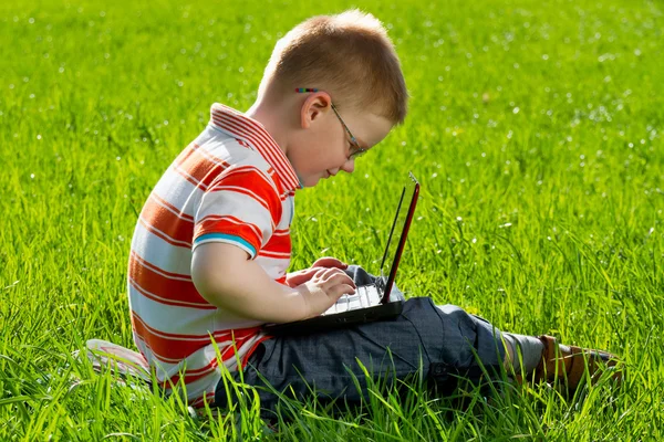 Хлопчик використовує свій ноутбук на відкритому повітрі в парку на траві — стокове фото
