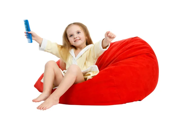 Kleines Mädchen sitzt auf einem Stuhl und kämmt die Haare mit Kamm — Stockfoto