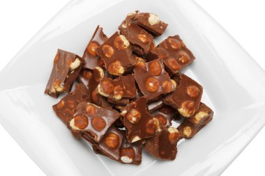 Broken chocolate pieces with nuts on white plate clipart