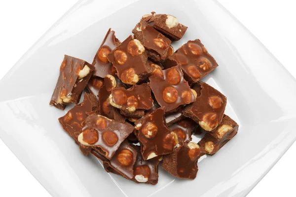 Broken chocolate pieces with nuts on white plate — Stock Photo, Image