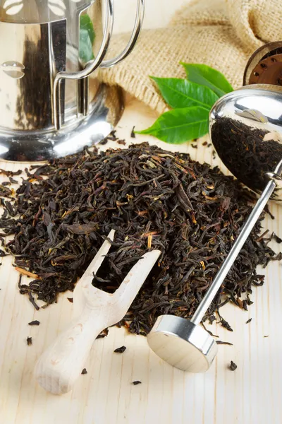 Black tea pile, teapot, wooden scoop — Stock Photo, Image