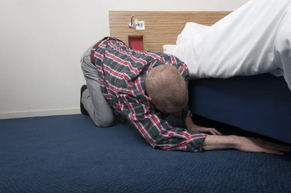 Człowiek wyszukiwania patrząc pod łóżkiem. Obrazek Stockowy