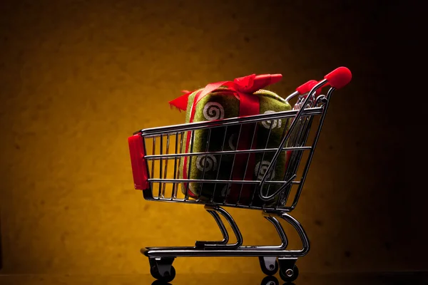 Carrinho de compras com presente no fundo amarelo — Fotografia de Stock