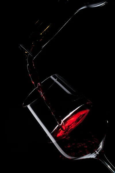 Vino tinto vertiendo en copa de vino aislado en negro — Foto de Stock
