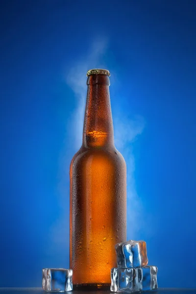 Koud bierfles met druppels, frost en damp op blauw — Stockfoto