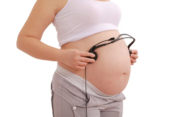 Беременная женщина с наушниками на животе — стоковое фото
