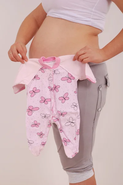 Bebek giysileri tutan hamile kadın — Stok fotoğraf