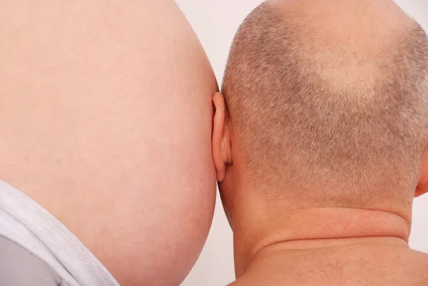 Man luistert naar de maag van de zwangere vrouw — Stockfoto
