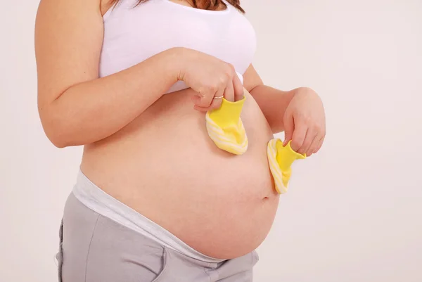 Těhotná žena hospodářství žluté botičky — Stock fotografie