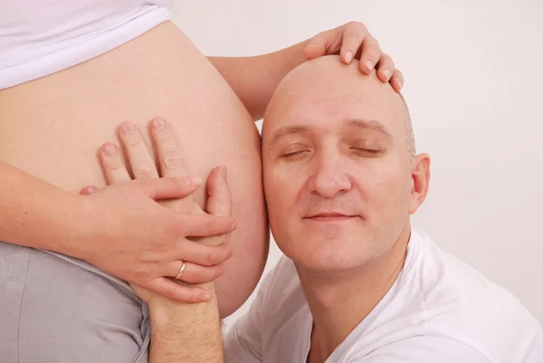 Man luistert naar de maag van de zwangere vrouw — Stockfoto