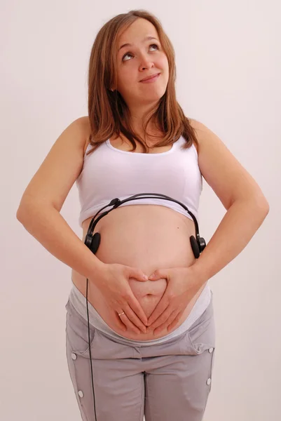 Mujer embarazada con auriculares en el estómago — Foto de Stock