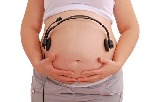 Donna incinta con le cuffie sullo stomaco — Foto Stock