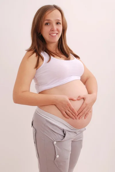 Těhotná žena spráskla ruce ve tvaru srdce — Stock fotografie