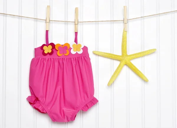 Baby baddräkt och sjöstjärna på ett klädstreck Stockbild