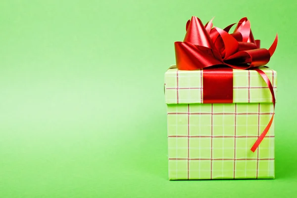Caja de regalo verde con cinta roja sobre fondo verde . — Foto de Stock