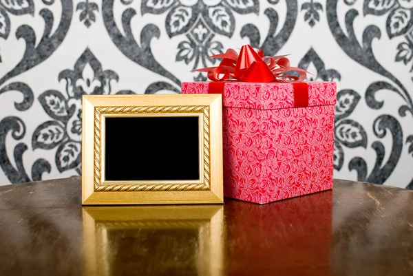 Golden photo frame and present box on table — Stockfoto
