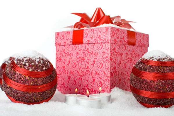 Christmas gift box in the snow with red balls and candles — Stock Photo, Image
