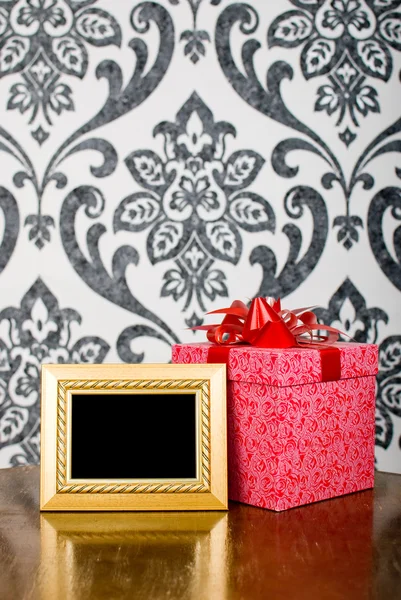 Moldura de foto dourada e caixa de presente na mesa — Fotografia de Stock