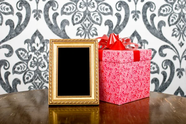 Moldura de foto dourada e caixa de presente na mesa — Fotografia de Stock