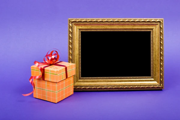 Gold photo frame and orange gift box with red ribbon on blue bac — Stock Photo, Image