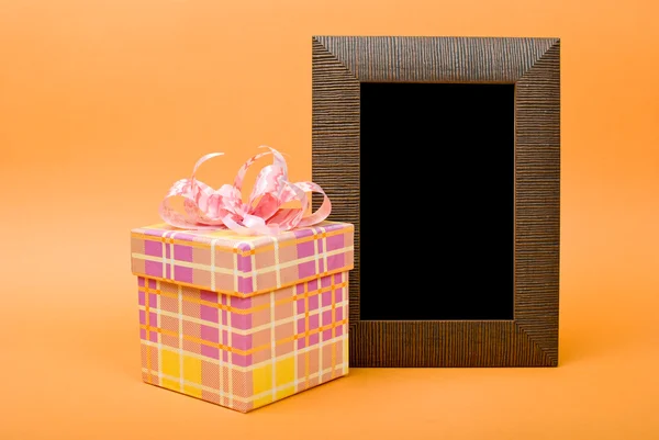 Ξύλο φωτογραφία πλαίσιο και κίτρινο κουτί δώρου με ροζ κορδέλα σε πορτοκαλί — Φωτογραφία Αρχείου