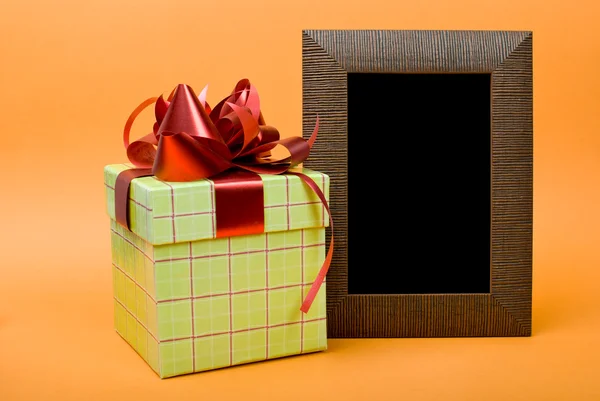 Ξύλο φωτογραφία κορνίζα και πράσινο κιβώτιο δώρων με κόκκινη κορδέλα σε πορτοκαλί ΒΑ — Φωτογραφία Αρχείου