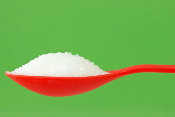 Spoon with sugar on green background — Stock Photo, Image