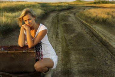 Pretty girl with a suitcase on a countryside road clipart