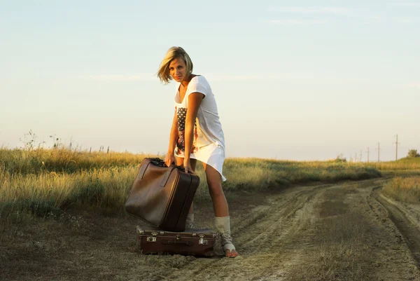 Bella ragazza con una valigia su una strada di campagna — Foto Stock