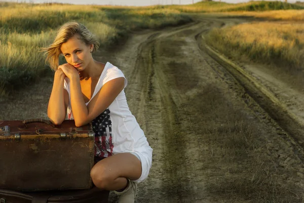 Красивая девушка с чемоданом на сельской дороге — стоковое фото