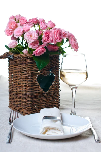Glas Weißwein und ein Korb mit Rosen — Stockfoto