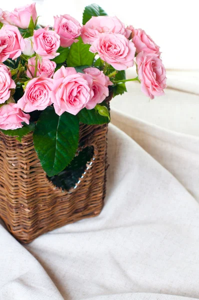 Rosa rosor i en flätad korg och linne tyg — Stockfoto