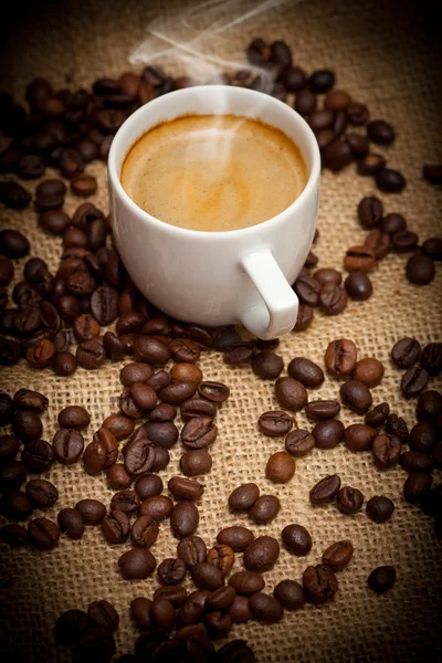 Primer plano taza de café caliente y granos de café —  Fotos de Stock