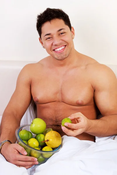 Portret atrakcyjny młody człowiek z owocami w łóżku — Zdjęcie stockowe