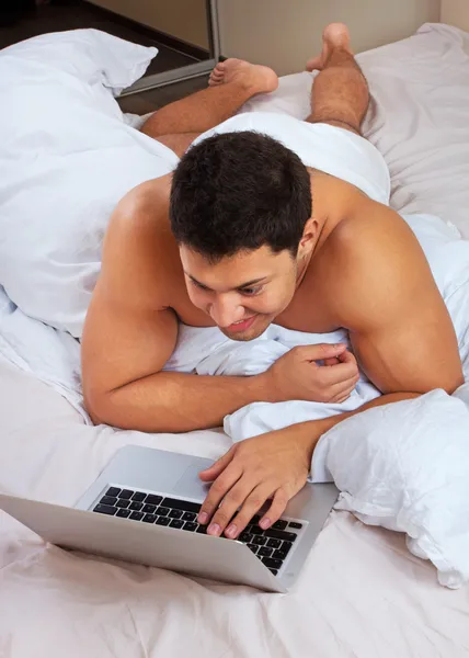 Yatmadan dizüstü kullanan genç adam — Stok fotoğraf