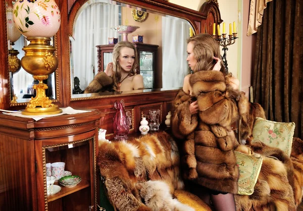 Kvinna i päls på spegeln i lyxig klassisk interiör. — Stockfoto