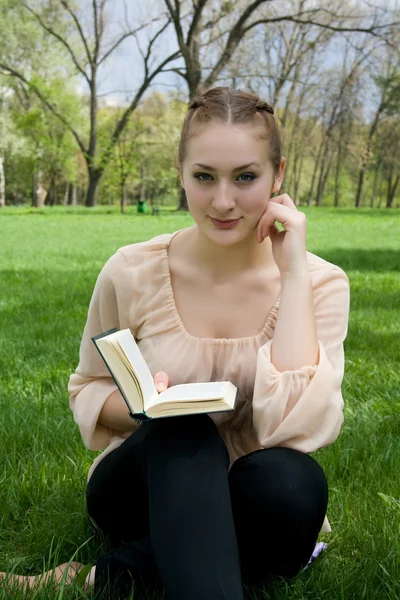 Jeune belle femme attentive se trouve sur l'herbe verte et lit livre — Photo