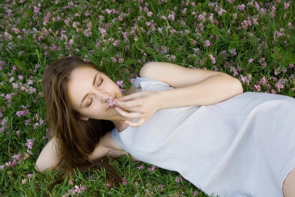 Hermosa chica acostada sobre hierba verde con flores y sosteniendo una f —  Fotos de Stock