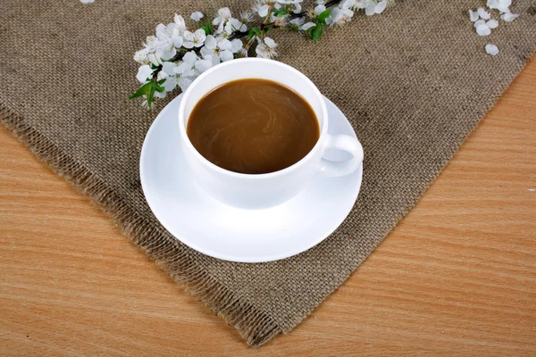 Φλιτζάνι καφέ με γάλα σε ένα πιατάκι και δαμάσκηνο λουλούδια — Φωτογραφία Αρχείου