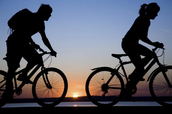 Jovem casal andar de bicicleta ao pôr do sol . — Fotografia de Stock