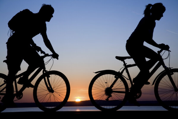 Young couple riding bicycles at sunset.
