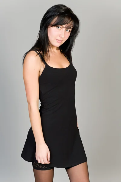 Aantrekkelijk meisje in een zwarte jurk op een grijze achtergrond — Stockfoto