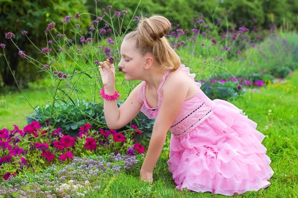 A menina bonita cheira flores na grama verde — Fotografia de Stock