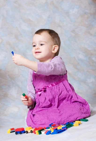 Het kind in een roze jurk met speelgoed — Stockfoto