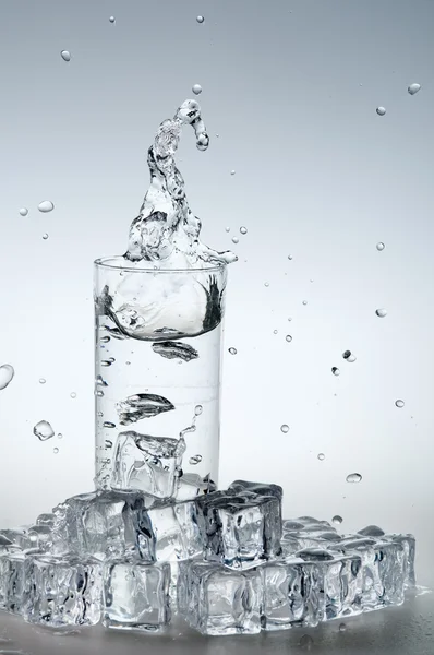 Mineral water splashing out from glass with ice cube. — Stock Photo, Image