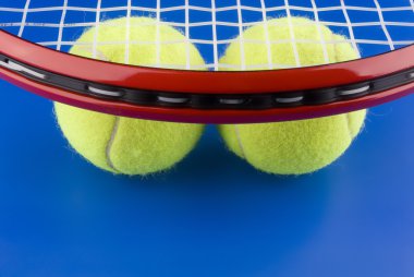 Tenis topları olan mavi bir arka plan üzerinde bir tenis raketi altında.
