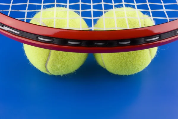 Pelotas de tenis está debajo de una raqueta de tenis sobre un fondo azul . — Foto de Stock