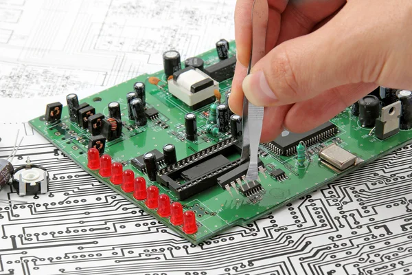 Uma mão com pinças segurando uma placa de circuito eletrônico em — Fotografia de Stock