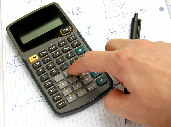 Wetenschappelijke calculator op notebookpapier en een hand — Stockfoto