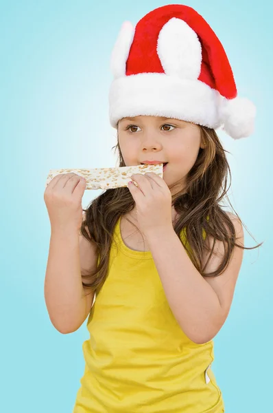Liten flicka klädd i rött santa hatt äta — Stockfoto